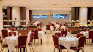 En rummelig restaurant med flere borde og stole, et buffetområde og udsigt til gaden gennem store vinduer.