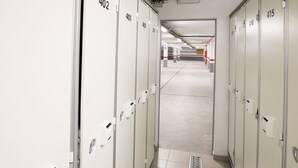 En gang med nummererede skabe, en rist på gulvet og en synlig udgangsdør.