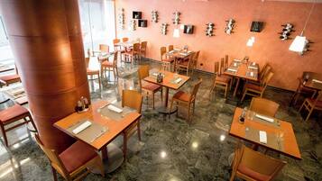 Un restaurante con varias mesas y sillas, suelo de mármol y una pared donde se exhiben botellas de vino.