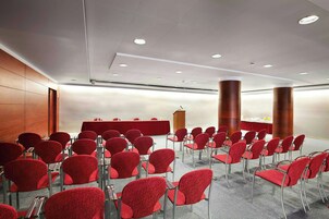 Un salón de conferencias con filas de sillas rojas, un atril y dos columnas cilíndricas grandes.