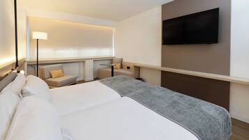 Ein Hotelzimmer mit einem großen Bett, einem an der Wand befestigten Fernseher, einer Couch und einem kleinen Tisch.