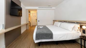Ein Hotelzimmer mit Bett, Wandfernseher, Nachttisch und Beistelltisch.