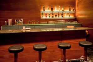 A bar area with a long counter, multiple bottles of liquor, and three stools. - Sercotel Delfos Andorra (Escaldes-Engordany)