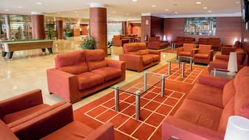 Un vestíbulo de hotel con varias zonas de estar, una mesa de billar y una recepción.