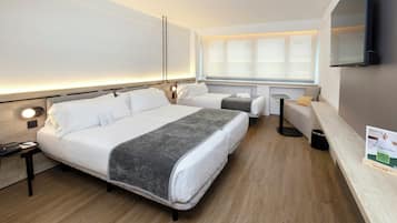 Habitación de hotel con una cama grande, mesitas de noche, un escritorio, una silla, un televisor y una ventana con persianas.