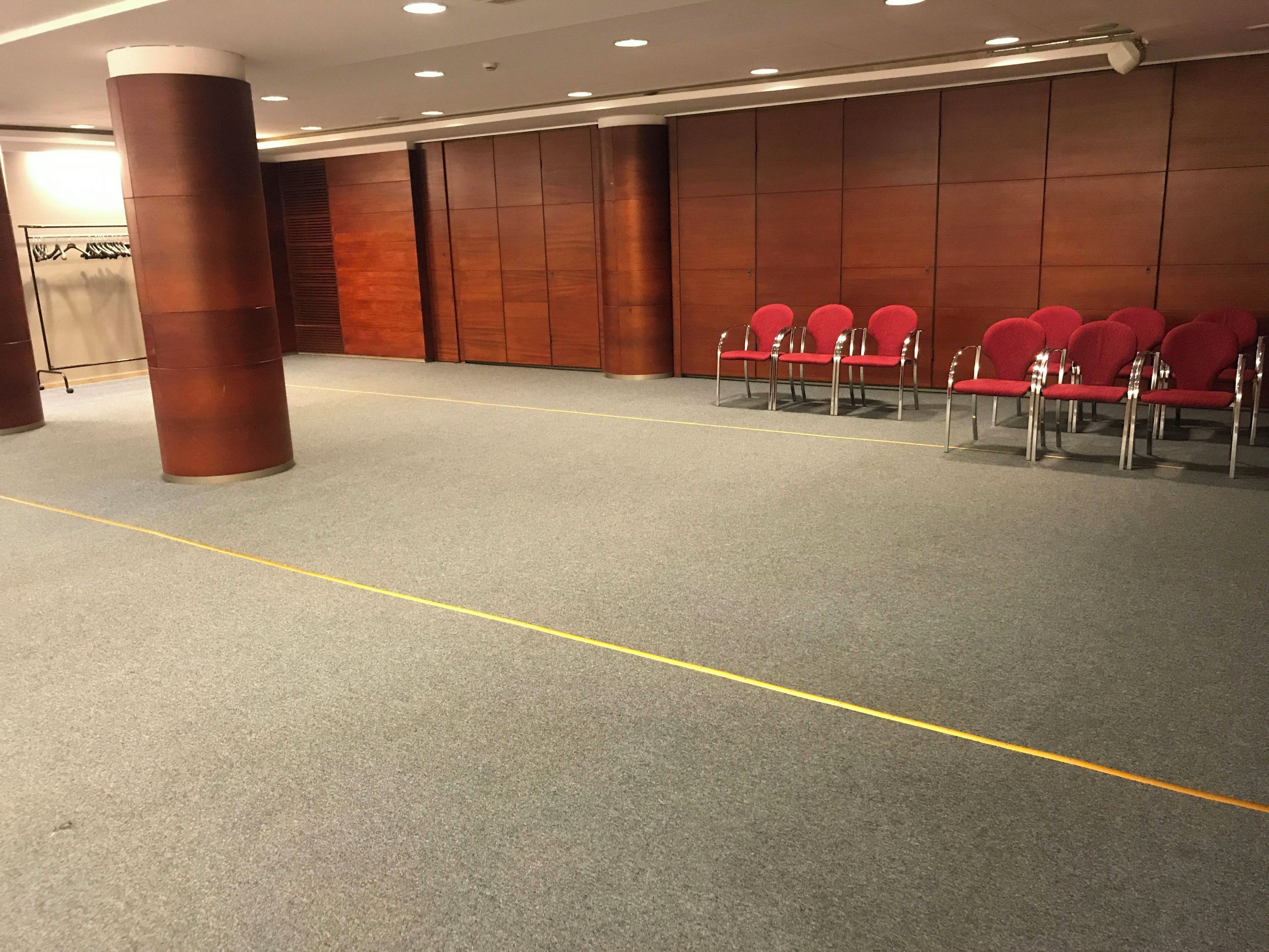 A conference room with a grey carpet, wooden panel walls, and red chairs arranged in rows.