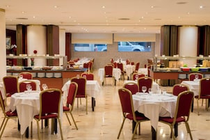Un restaurante amplio con varias mesas y sillas, una zona de bufé y un gran ventanal con vistas al exterior.