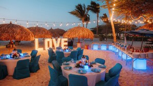 An outdoor dining area with round tables, blue chairs, and thatched umbrellas. - Amsterdam Manor Beach Resort (Noord)