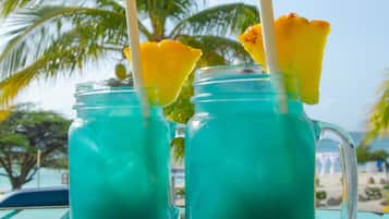 Deux boissons turquoise, servies avec des pailles et des morceaux d’ananas, sur une table de plage.