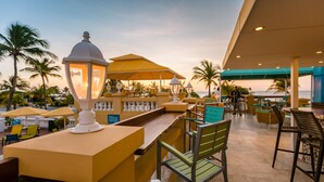 Un espacio al aire libre con mesas, sillas y sombrillas, con vista a la playa.