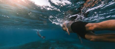 An underwater view of a swimmer with a clear view of the ocean floor and another swimmer in the distance.