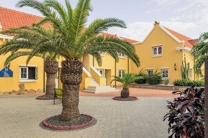 Un patio con palmeras, un edificio amarillo con tejas rojas y una escalera que lleva a una puerta.