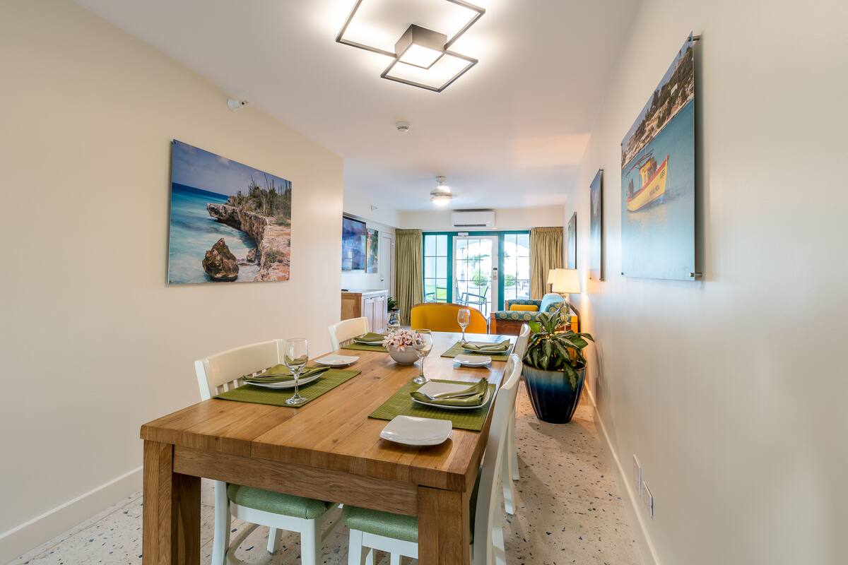 A dining area with a wooden table set for four, white chairs, and a potted plant.