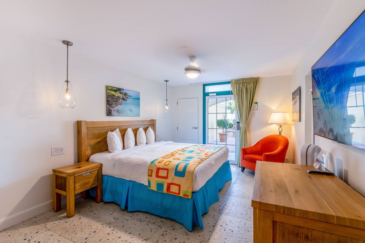 A bedroom with a bed, a wooden nightstand, a desk, a chair, and a window with curtains.