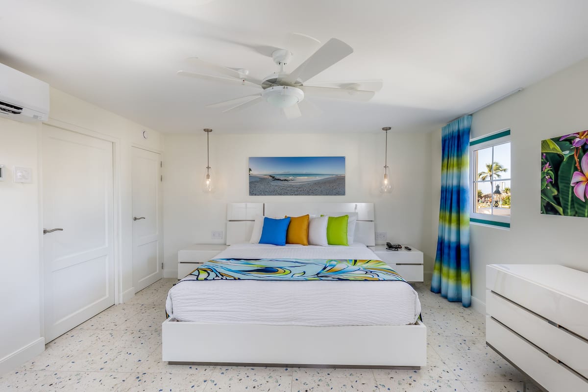 A bedroom with a bed, a ceiling fan, a nightstand, a dresser, and a window with curtains.