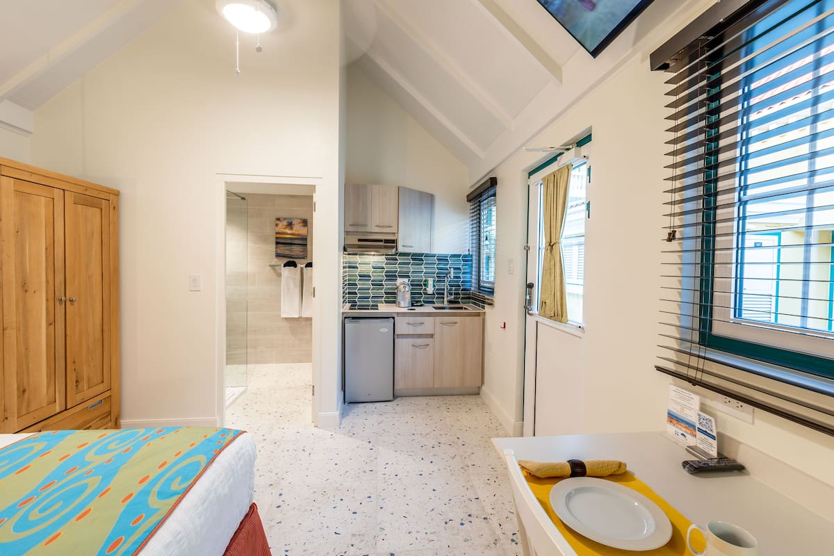 A compact hotel room with a kitchenette, a bathroom with a bathtub, and a wooden wardrobe.