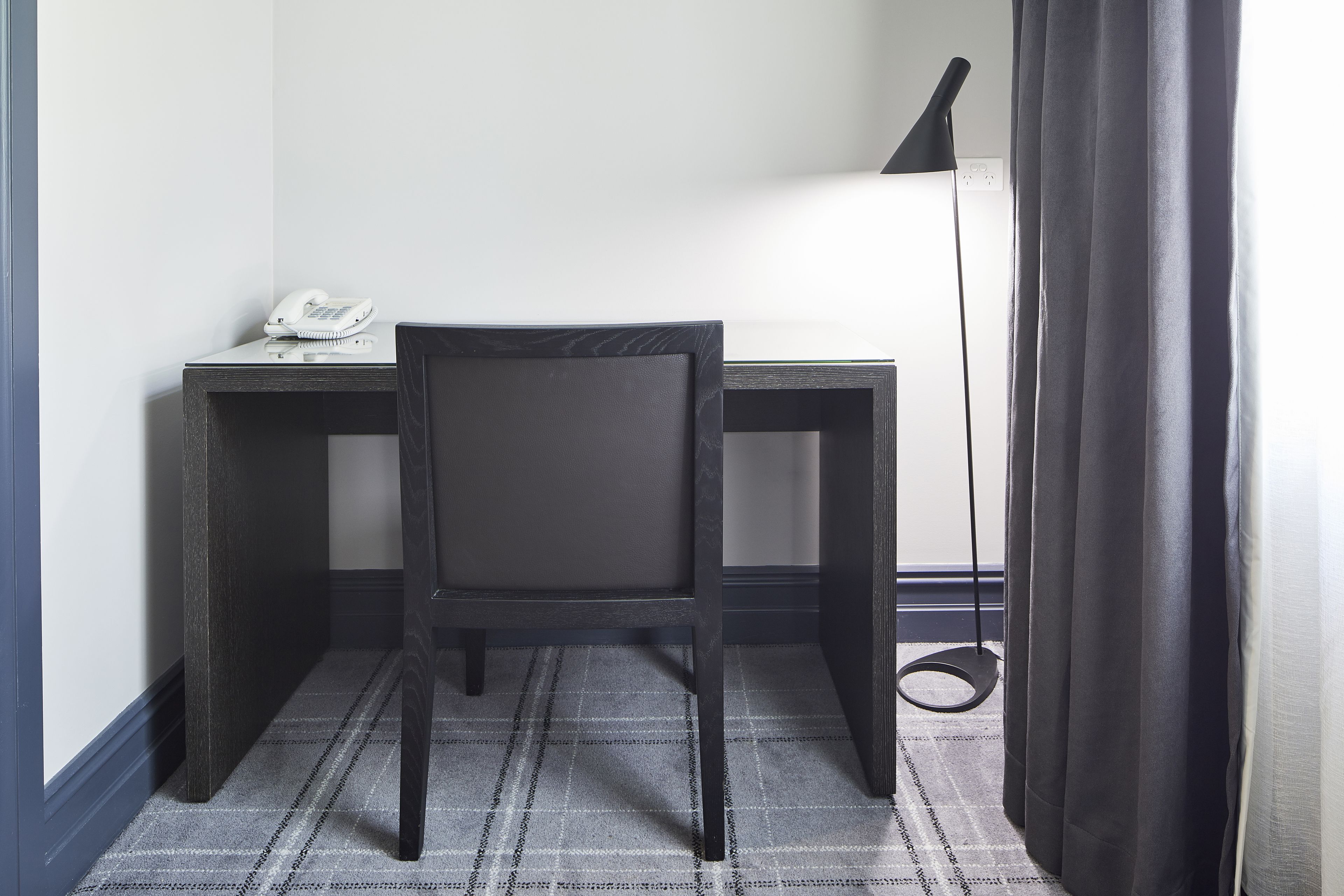 A small, dark wooden desk with a telephone and a lamp.