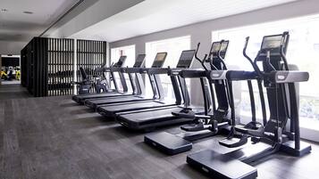 A row of treadmills in a gym with a modern design, large windows, and a dark wooden floor.