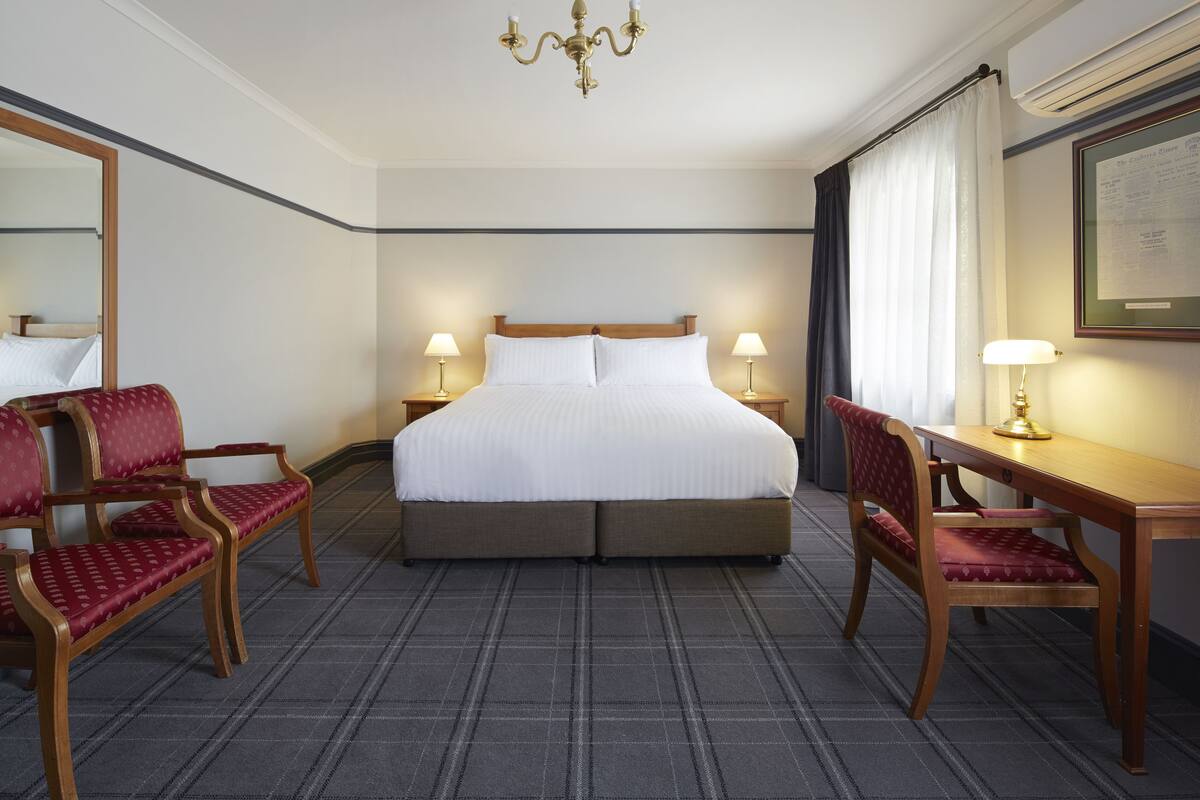 A hotel room with a large bed, two bedside tables with lamps, a desk with a chair, and a large mirror.