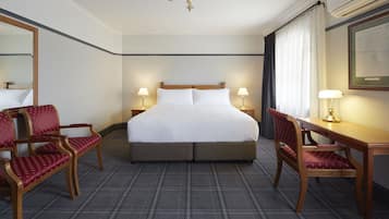 Una habitación de hotel con una cama grande, dos mesitas de noche con lámparas, un escritorio con silla y un espejo amplio.