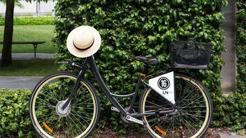 A stationary bicycle with a basket and a number plate, parked against a hedge.