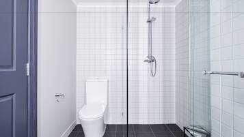 A modern bathroom with a glass shower enclosure, a white toilet, and a tiled floor.
