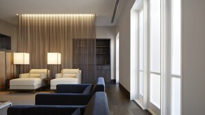 A modern hotel room with a seating area featuring two armchairs and a sofa, a large window, and a built-in shelving unit. - Brassey Hotel (Barton)