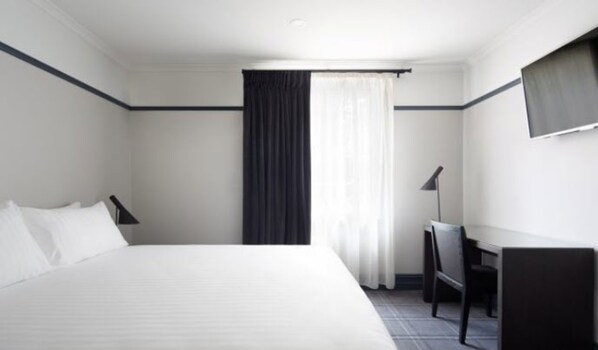 A hotel room with a large bed, a desk, a chair, and a TV on the wall.