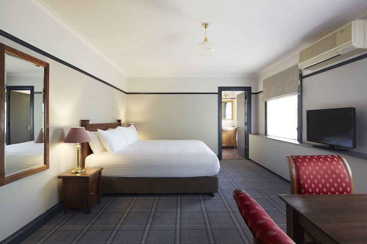 A hotel room with a bed, bedside lamp, TV, and a red chair.