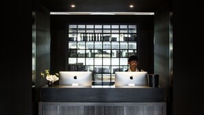 A reception desk with two laptops, a vase with flowers, and a view of a building through a window. - Brassey Hotel (Barton)
