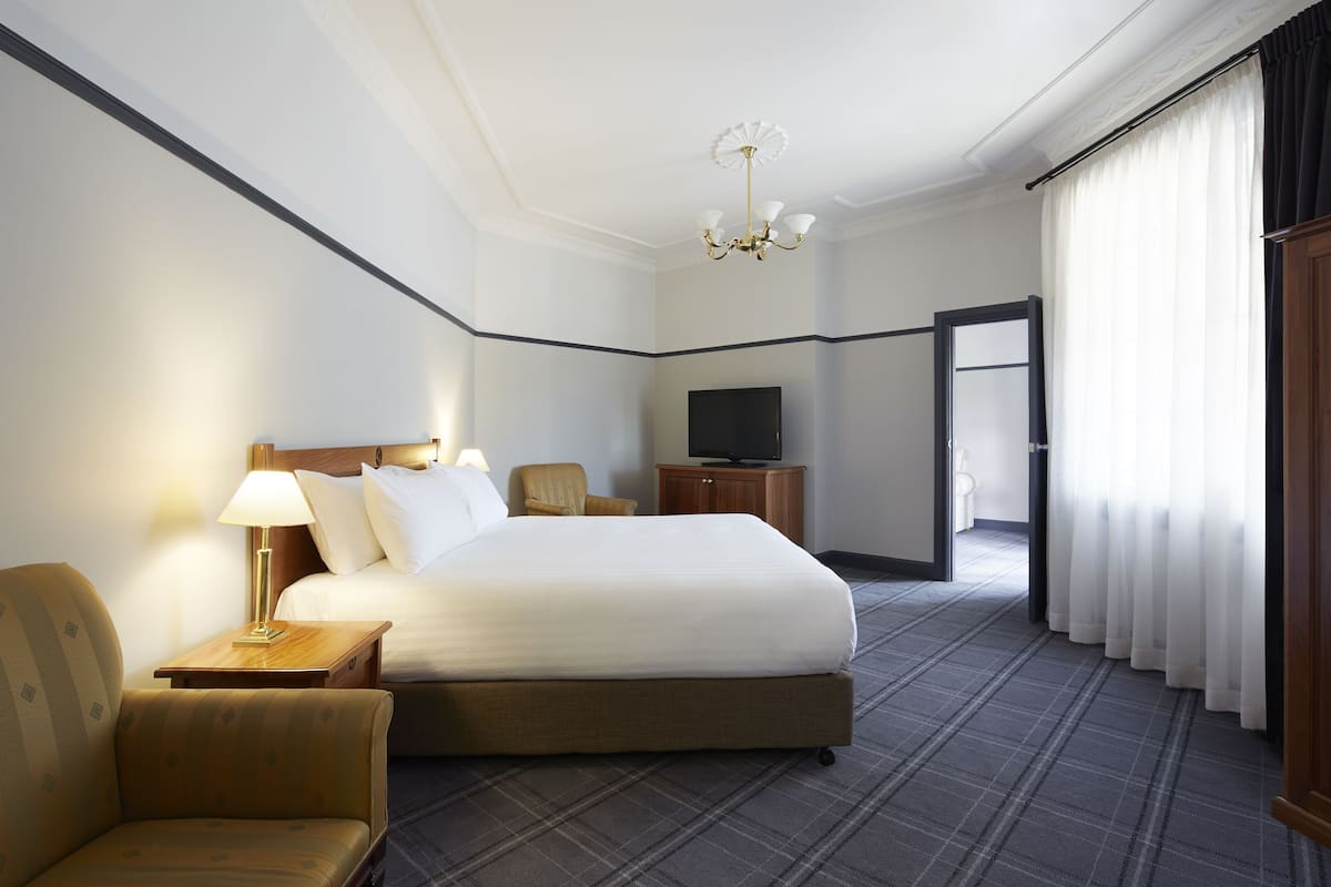 A hotel room with a large bed, a television, a wooden nightstand, a chair, and a carpeted floor.