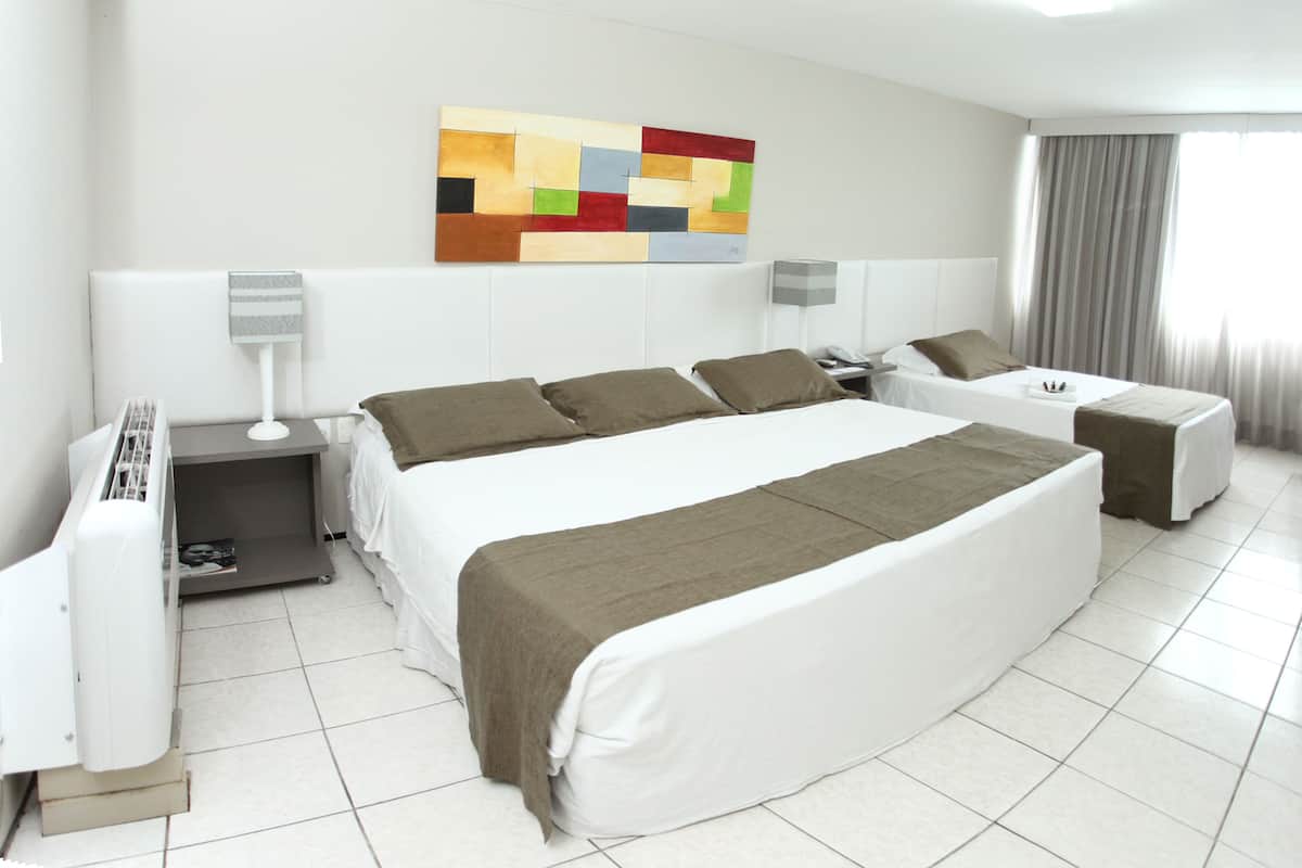 A hotel room with a large bed, two bedside tables, a desk, and a chair. There is a colorful abstract painting on the wall and a window with curtains.
