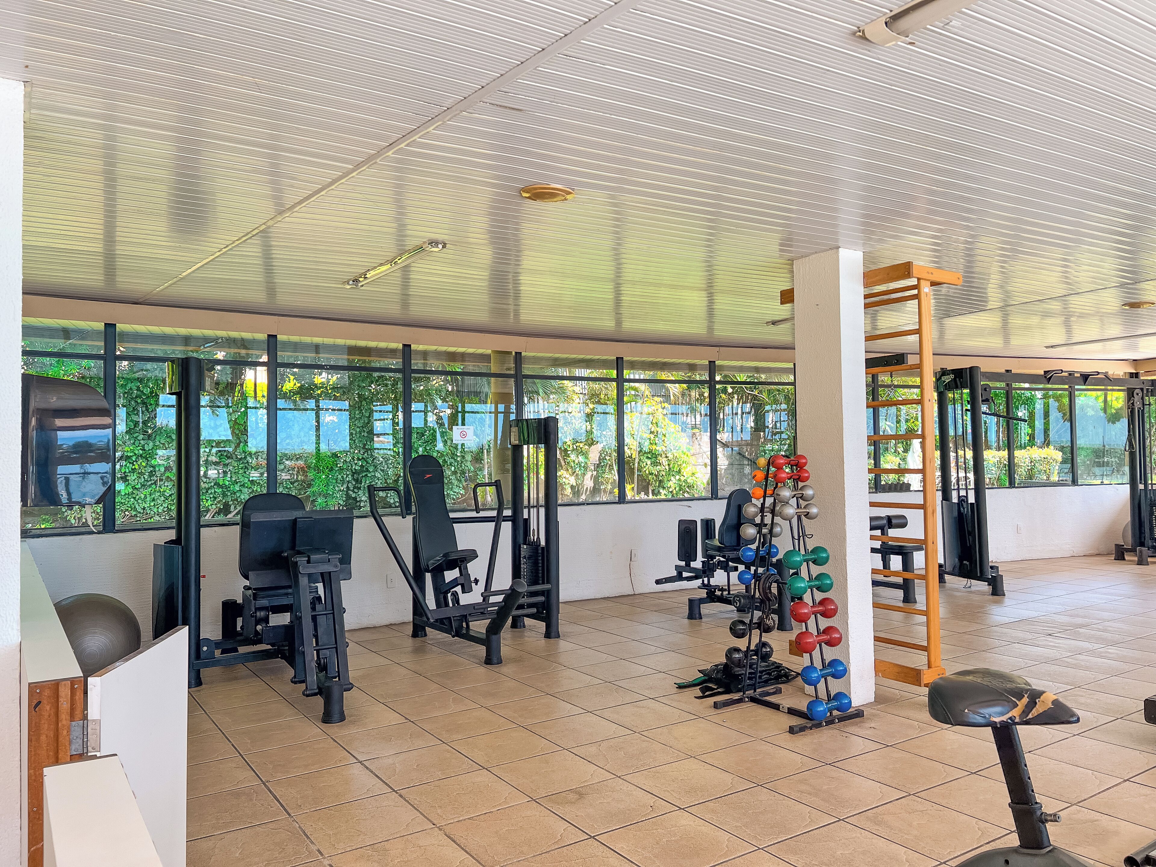 A gym with various exercise equipment, large windows, and a tiled floor.