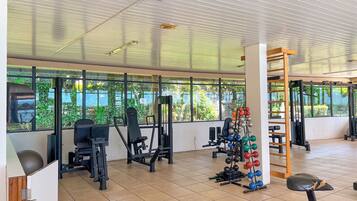 A gym with various exercise equipment, large windows, and a tiled floor.