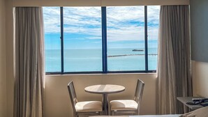 A hotel room with a large window, a bed, a small round table with two chairs, and a bedside table with a phone. - Marina Park (Fortaleza)