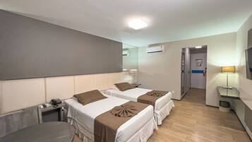 Quarto de hotel com duas camas, uma escrivaninha, uma cadeira, um abajur e um espelho.