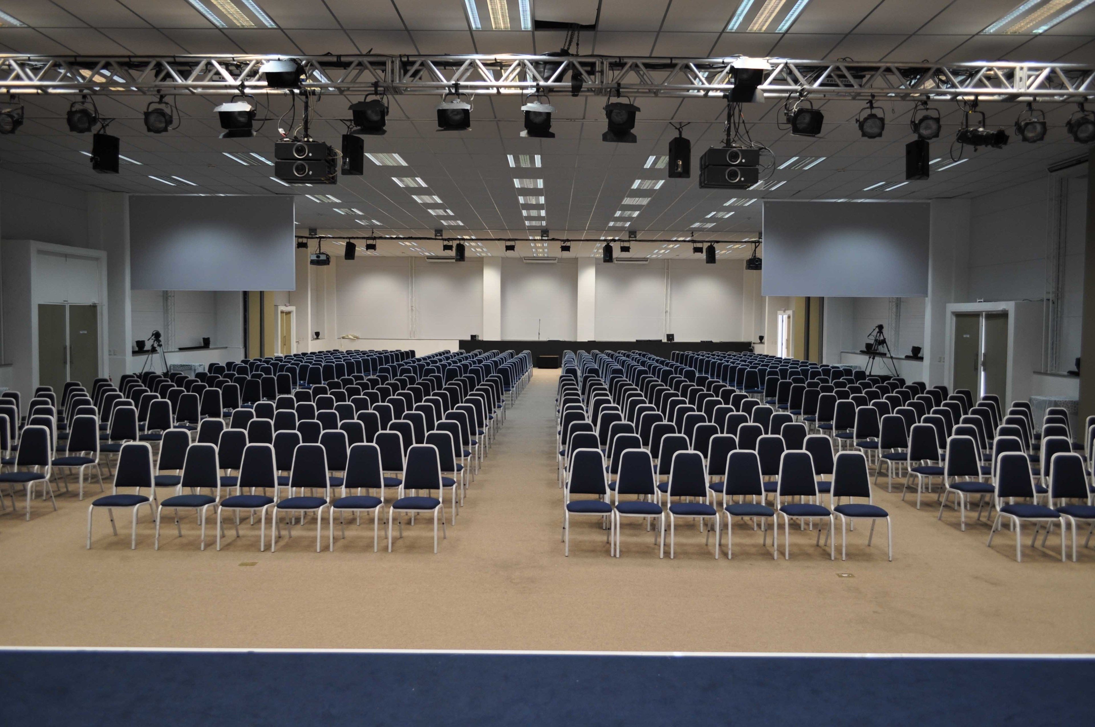 Un amplio salón de conferencias con filas de sillas y un escenario con equipo de iluminación.