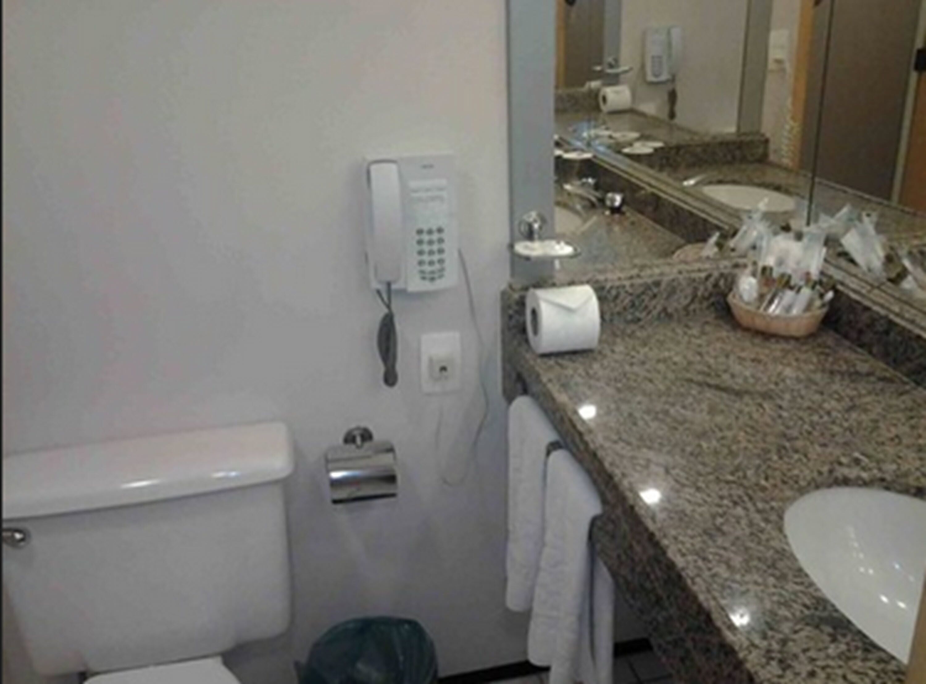 Un baño con inodoro, lavamanos, espejo, teléfono y toallero.