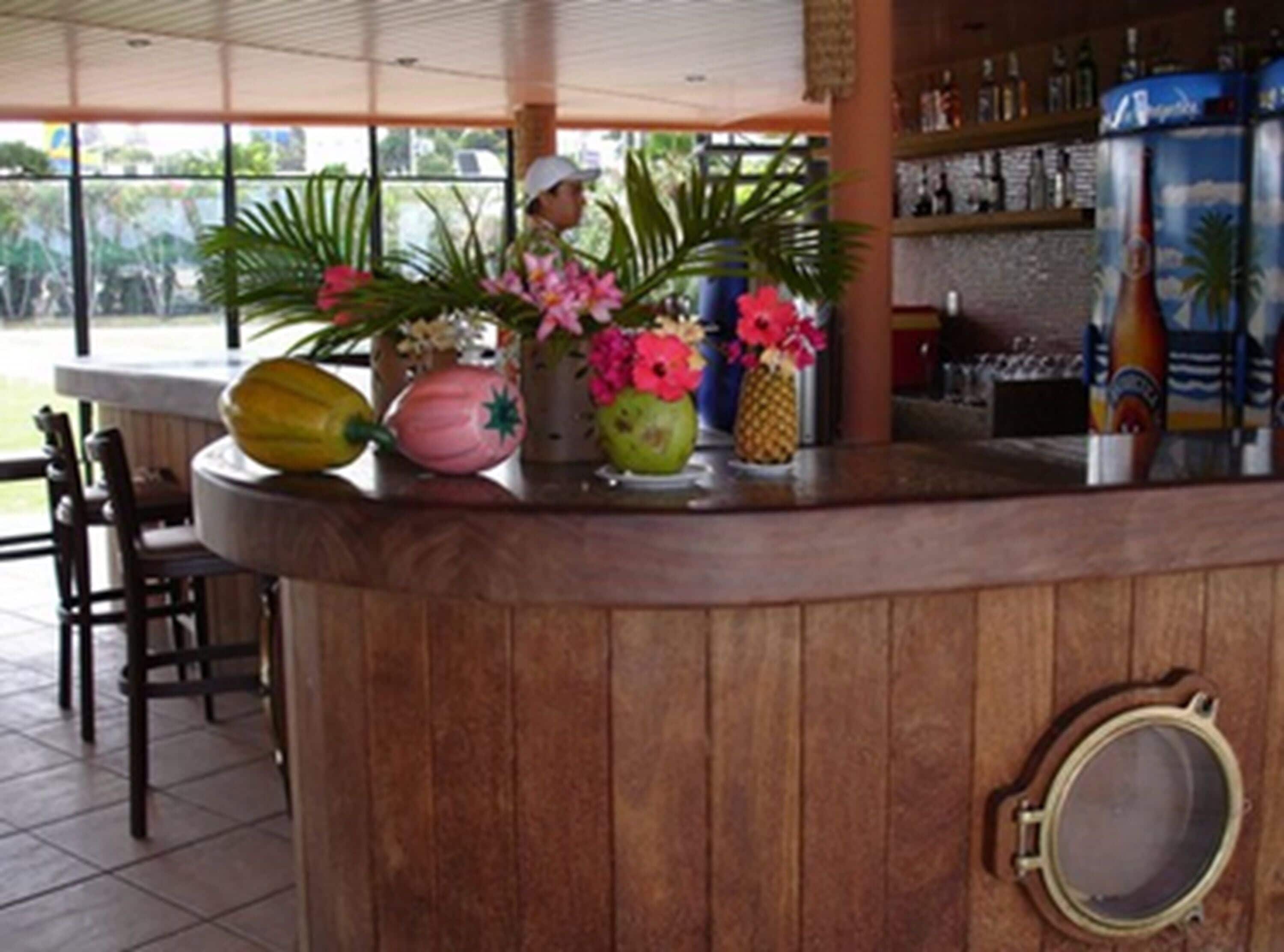 Uma área de bar com balcão de madeira, vários vasos em formato de frutas e uma grande janela com vista para o exterior.