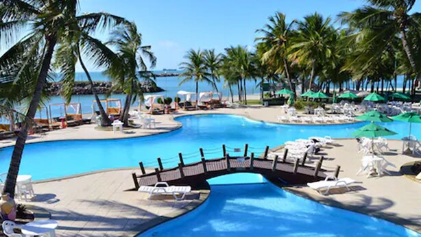 A swimming pool with a bridge, palm trees, lounge chairs, and umbrellas. - Marina Park (Fortaleza)