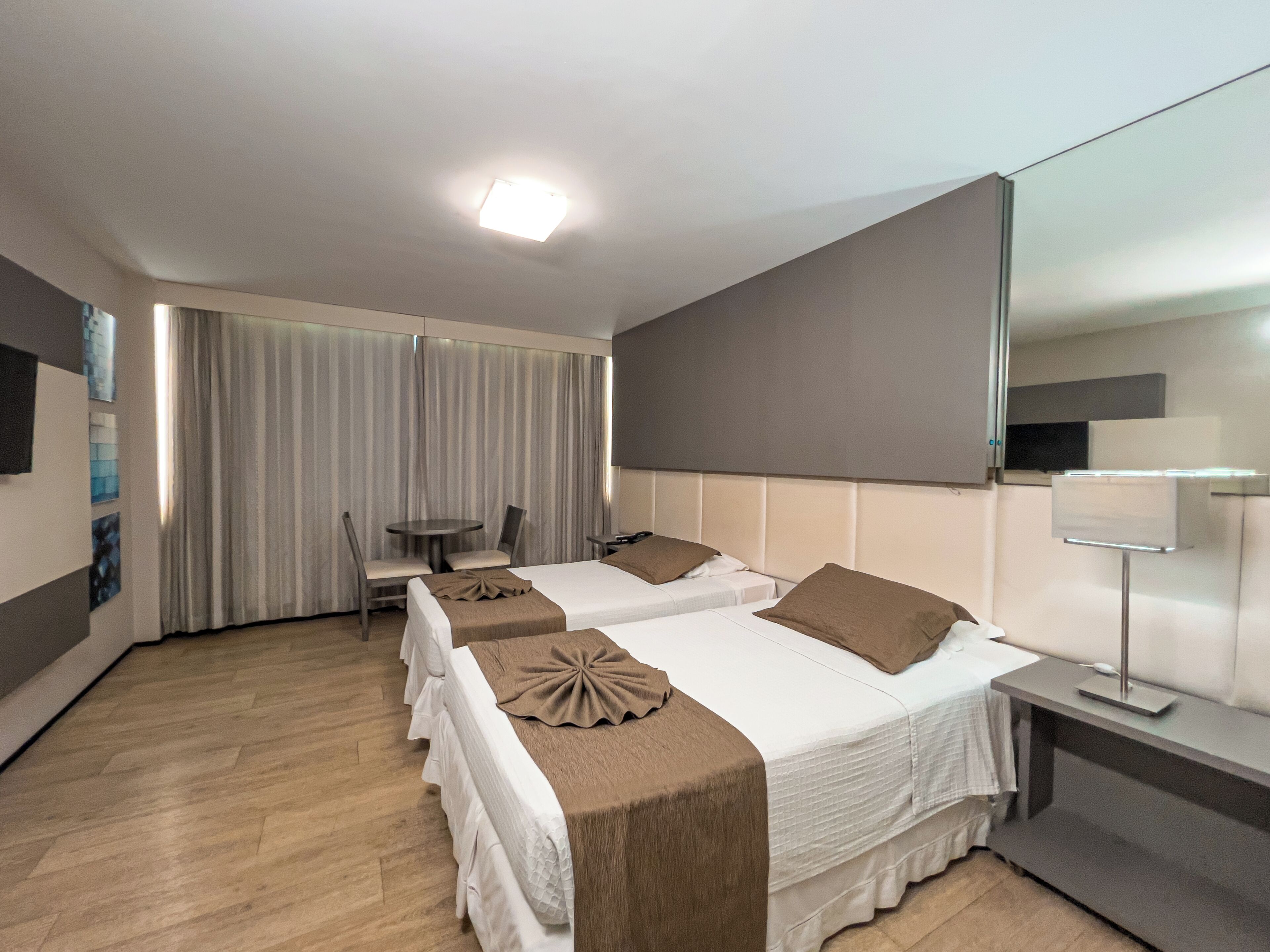 Una habitación de hotel con dos camas, un escritorio, una silla, un espejo y una ventana con cortinas.