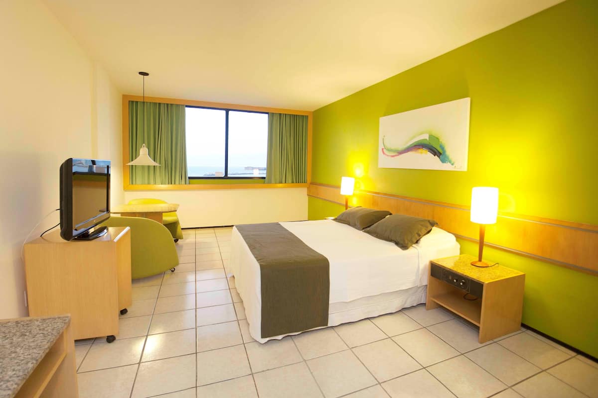A hotel room with a bed, bedside lamps, a desk with a television, and a window with curtains.