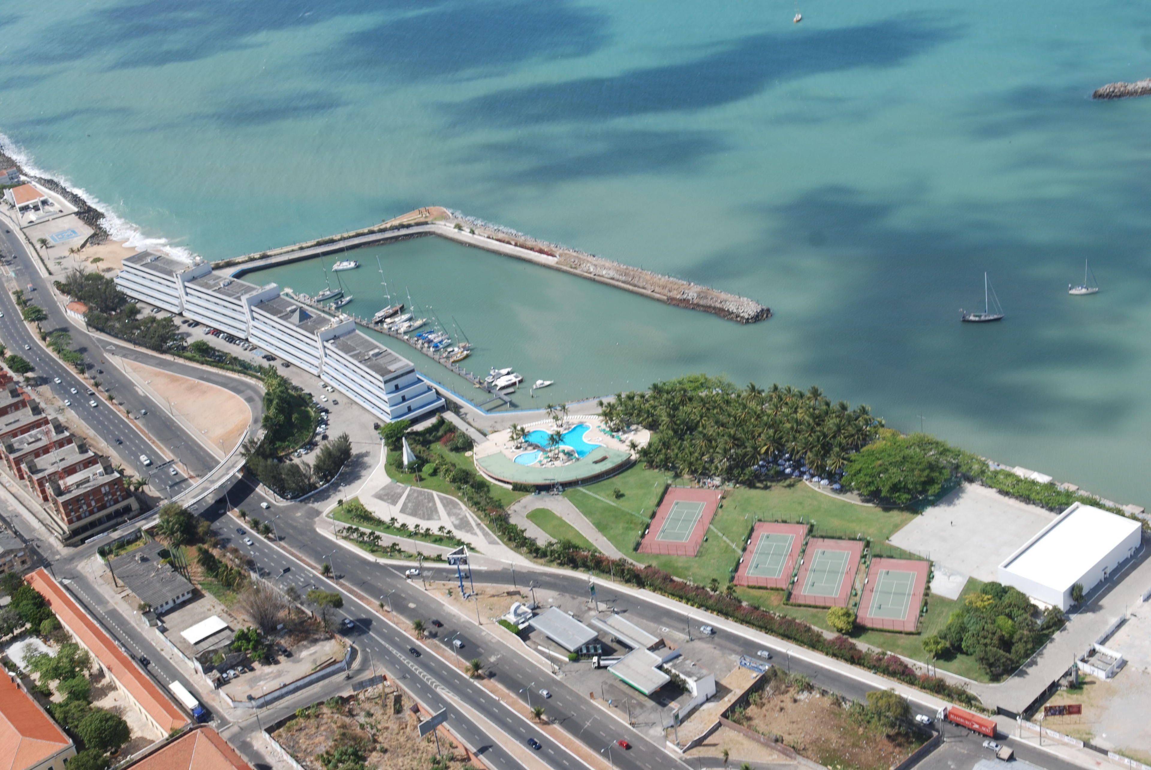 Vista aérea de uma área costeira com um porto de iates, instalações esportivas e um edifício grande.