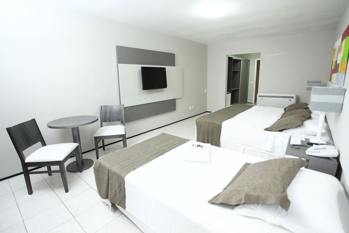 A hotel room with two beds, a desk, a chair, a TV, and a wardrobe.