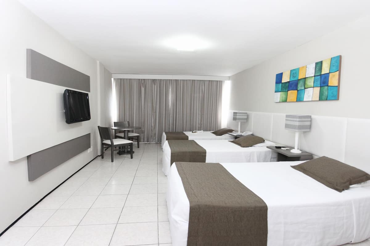 A hotel room with two beds, a TV, a desk with a chair, and a window with curtains.