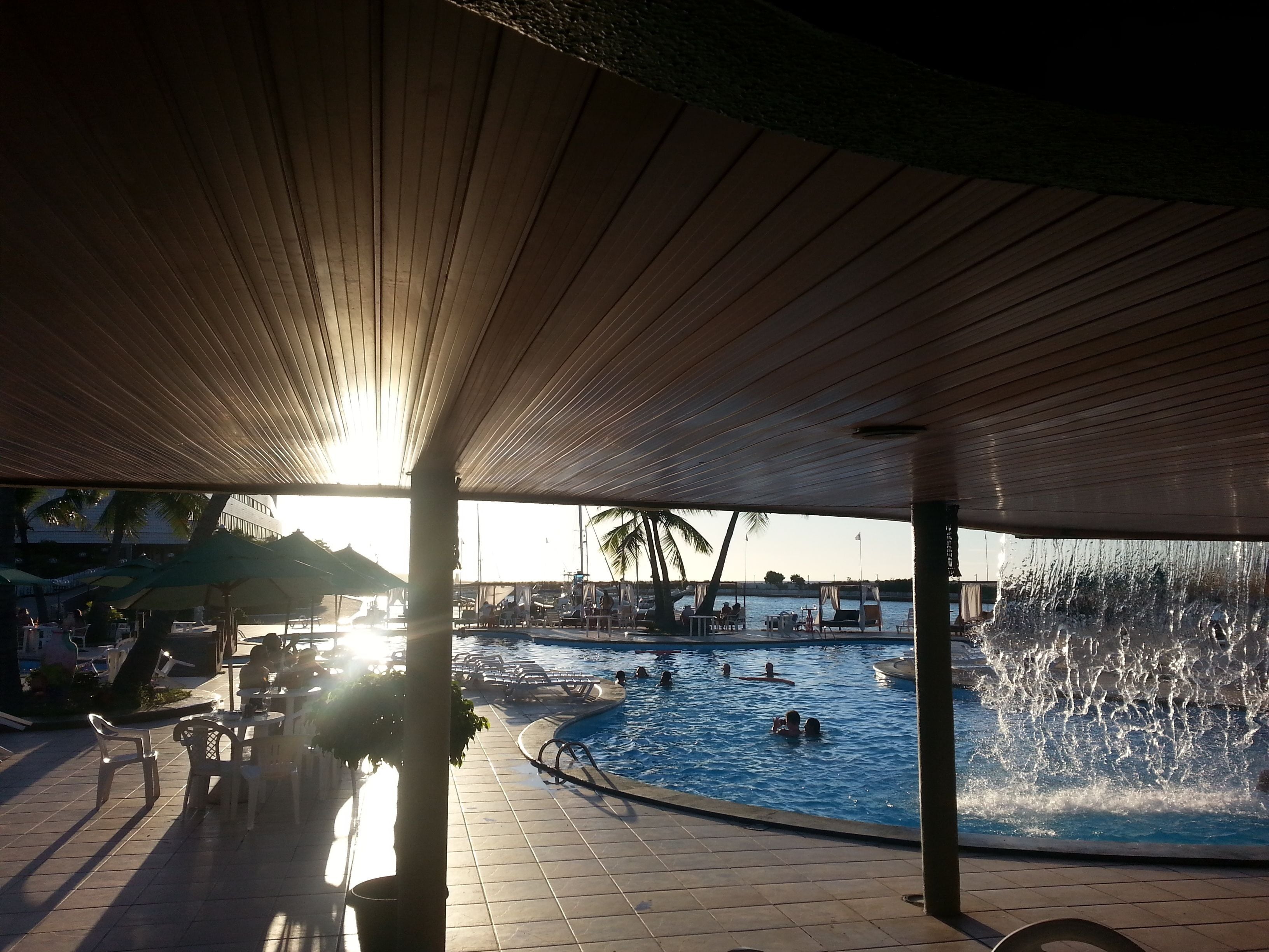 A pool area with a covered seating area and a view of the water.