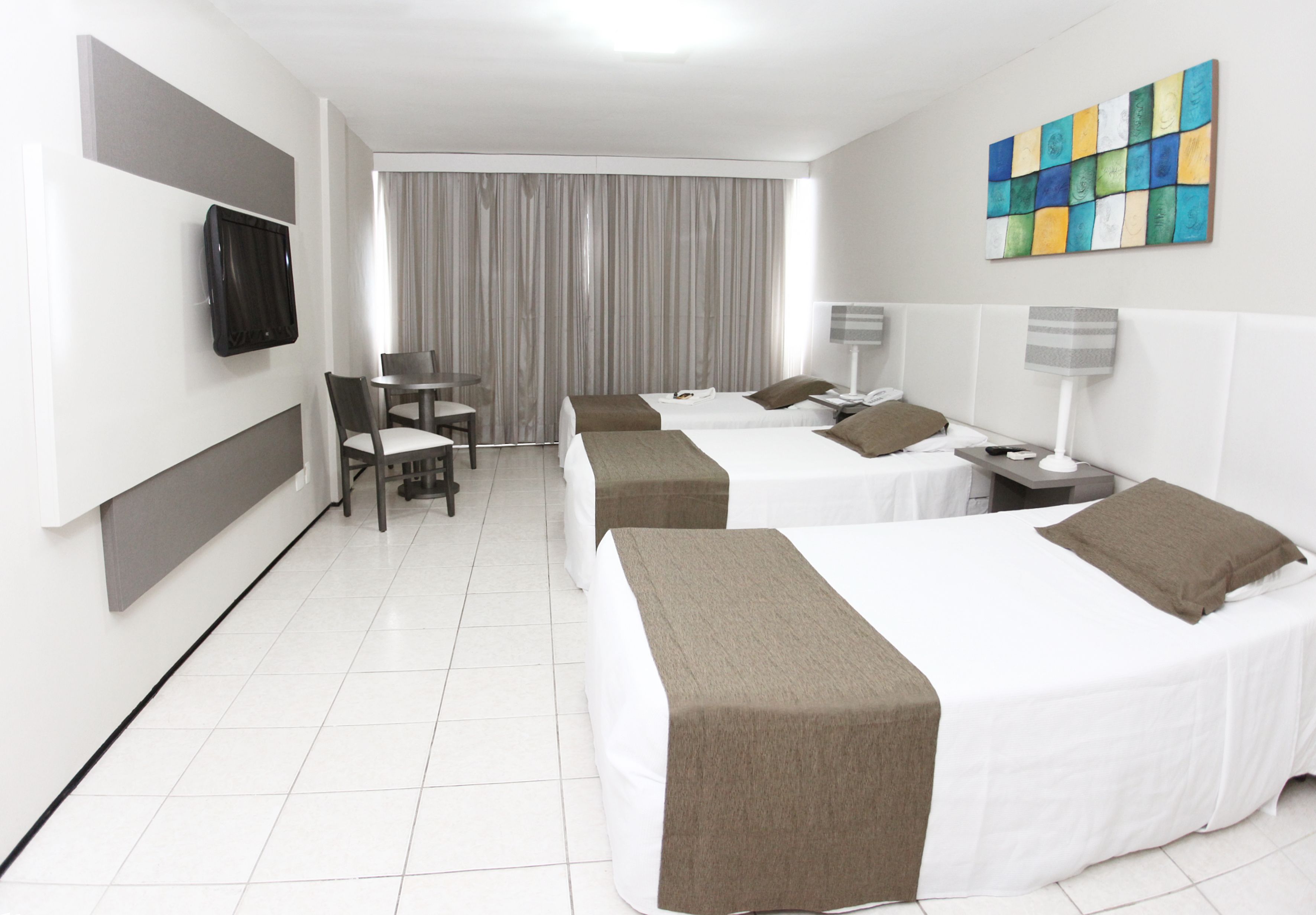 Quarto de hotel com duas camas, uma escrivaninha, uma cadeira, televisão e um quadro na parede.