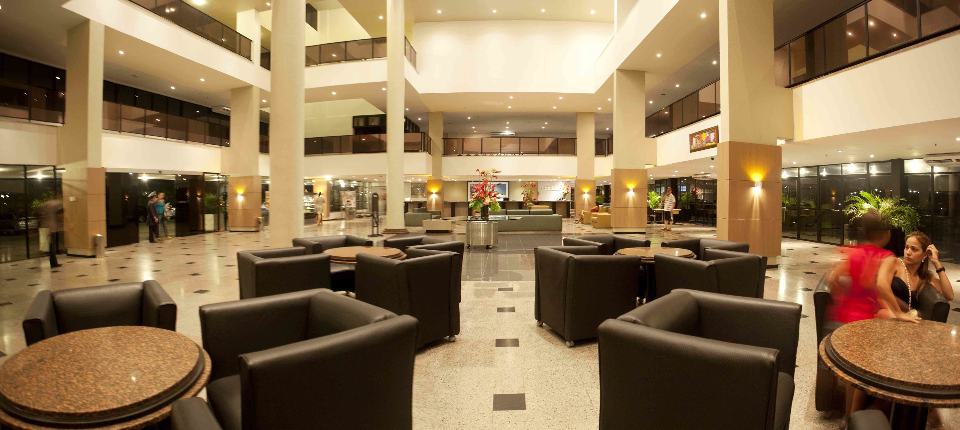 A spacious lobby with multiple seating areas, a central reception desk, and a high ceiling with natural light.