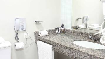 Un baño moderno con encimera de granito, lavabo blanco y un espejo grande. Hay dos teléfonos instalados en la pared, un perchero y un inodoro.