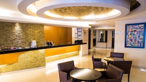 Un vestíbulo de hotel con mostrador de recepción, zona de estar y techo decorativo.